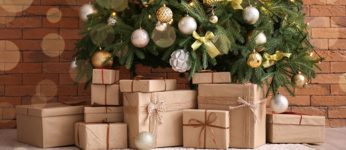 The lower half of a decorated Christmas tree against a brick wall with gifts below wrapped in brown paper with string.