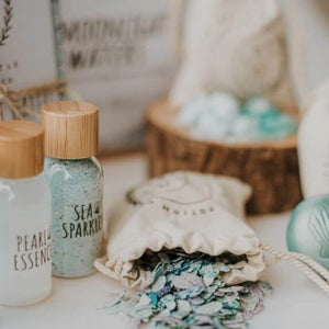 Two clear bottles labeled "Pearl Essence" and "Sea Sparkles" sit beside a pouch with a flaky, glittery ingredient spilling out.