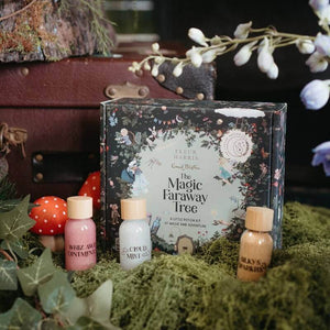 The Magic Faraway Tree Mindful Magic Potion Kit, featuring a floral illustrated box surrounded by the bottles of shimmery liquid and small mushroom decorations, styled on moss with leaves and a vintage suitcase in the background.
